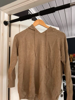 Beige hoodie - En stilren beige hoodie med huva och dragsko. Tillverkad i ett mjukt, tunt material som känns skönt mot huden. Hoodien har långa ärmar och ribbade muddar vid ärmslut och nederkant. Perfekt för en avslappnad och enkel look.