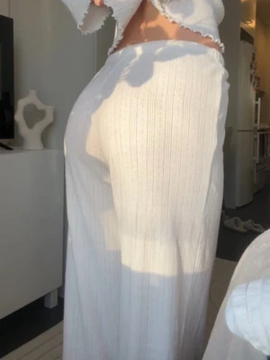 Vita ribbade mjukisbyxor med dragsko - Säljer ett par vita mjukisbyxor med ribbat tyg och raka ben. Byxorna har en bekväm resår i midjan med dragsko för justerbar passform. Perfekta för en chill och avslappnad stil. Materialet ser mjukt och stretchigt ut.