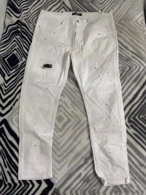 Balmain jeans - Säljer ett par vita jeans med slim fit och coola slitningar samt svarta färgstänk på framsidan. Jeansen har klassisk femficksdesign och raka ben. Perfekta för dig som gillar en edgy och trendig stil. Pris ka diskuteras