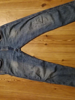 Replay jeans med slitningar - Snygga blå anbass jeans med lätt slitna detaljer och klassiska fem fickor. Jeansen har en något tvättad look och raka ben. Perfekta för en avslappnad stil och passar till det mesta. Materialet är denim i bomull. 10/10 skick! 