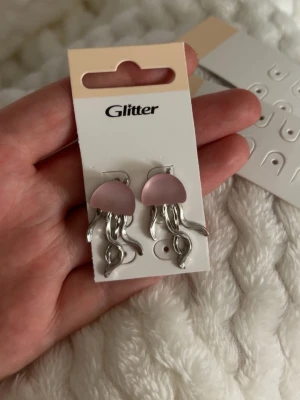 Rosa manetörhängen  -  örhängen formade som maneter med rosa kupol och silverfärgade tentakler. Jag köpte ett helt sett men aldrig använt domhär och kommer nog aldrig använda dom, som du kan se på bild så har jag då klippt bort dem andra hålen så slipper du få hela dem andra tomma sidorna