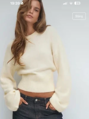 Krämvit stickad tröja från Gina Tricot - Säljer en krämvit stickad tröja från Gina Tricot med rund hals och bred ribbstickad nederkant. Tröjan har långa, lite puffiga ärmar och är tillverkad i mjukt material som känns skönt mot huden. Perfekt för lager-på-lager och snygg till jeans.