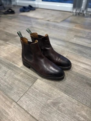  Ralph Lauren Chelsea boots  - Säljer ett par klassiska mörkbruna Ralph Lauren Polo Chelsea boots i slätt läder med elastiska paneler på sidorna och gröna dragflikar bak. Storlek 45. Toppskick (använda 3-4ggr). Äkta kvalitets läder. Mjuk och skön innersula. Perfekta för dig som gillar stilrena och tidlösa skor. Kolla även in mina andra plagg för bundle rabatter 