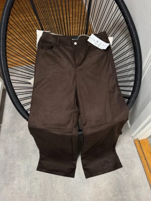 Mörkbruna byxor i fejkskinn Gina Tricot - Mörkbruna byxor från Gina Tricot i fejkskinn med midjehög passform. Byxorna har klassisk femficksdesign, bälteshällor och raka ben. Perfekta för dig som vill ha en trendig och stilren look.