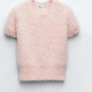 Ljusrosa fluffig stickad tröja Zara - Supersöt ljusrosa stickad tröja från Zara med korta ärmar och fluffig, mjuk textur. Tröjan har rund halsringning och en croppad passform som ger en trendig look. Perfekt för dig som vill ha något extra mysigt och stylish.