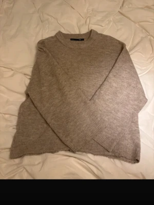 Beige stickad tröja från 157 - Mysig beige stickad tröja från 157 med rund halsringning och ribbade muddar vid ärmslut och nederkant. Tröjan har en enkel och avslappnad passform, perfekt för lager på lager. Materialet känns mjukt och behagligt mot huden.