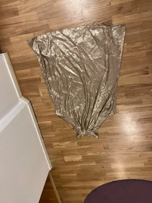 Glittrig guld kortklänning 2XL - Säljer en glittrig guld kortklänning i storlek 2XL. Klänningen har en lös passform och är tillverkad i ett skimrande syntetmaterial. Perfekt för dig som vill sticka ut med metallic-look och enkel siluett.