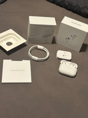 Airpods pro 2 ANC - Apple AirPods Pro i vit färg med trådlöst laddningsetui. Snygg och kompakt design i plast, levereras med originalkartong, USB-C laddkabel och extra öronproppar. Perfekta för dig som vill ha brusreducering och grymt ljud i ett smidigt format.