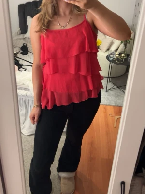 Röd/Rosa volangig linnetopp - Snygg röd linnetopp med flera lager volanger och tunna axelband. Perfekt för dig som vill sticka ut lite extra. Luftig och lätt, passar bra till både jeans och kjol.