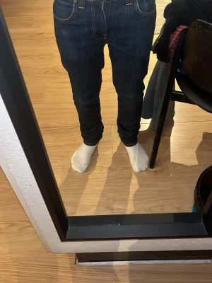 Mörkblå jeans från Nudie Jeans - Snygga mörkblå jeans från Nudie Jeans med raka ben och klassiska kontrastsömmar. Jeansen har fem fickor och ikonisk brodyr på bakfickorna. Tillverkade i denim av bomull för en tidlös look.