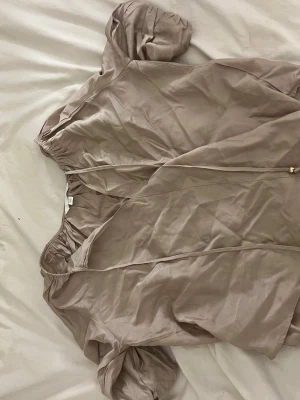 Beige blus med puffärm och knyt - Snygg beige blus med puffärmar och knytband med gulddetaljer. Blusen är på bilden ostruken och blir finare när den är struken🤗!!Om du köper välj gärna att hämta vid upphämtningsställe då det blir enklare för mig att posta på det viset!!