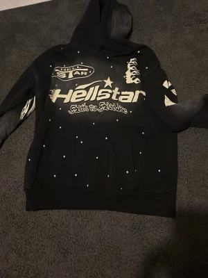  Dödscool Hellstar hoodie svart/vit - Säljer en svart hoodie från Hellstar med stora vita tryck fram och bak, inklusive flames, stjärnor och logga. Hoodien har huva där foder och utsida är i samma färg, samt känguruficka framtill. Materialet är mjukt och bekvämt, perfekt för streetwear. Kan bara ses i Stockholm 