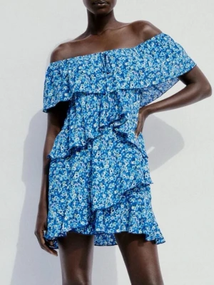 Blå blommig offshoulder klänning från Zara - Superfin blå offshoulder-klänning i blommigt mönster i blått och vitt, volangdetaljer samt ett knyte vid bröstet. Klänningen har även inbygga shorts men som ej syns! Har knappt används. Säljs inte längre🩷