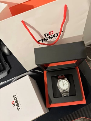 Tissot silverfärgad klocka - Stilren klocka från Tissot med silverfärgat armband i metall och vit urtavla. Klassisk rund form och minimalistisk design, perfekt för dig som gillar tidlösa accessoarer. Kommer i originalask och med Tissot-påse.