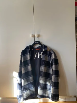 Rutig jacka Selected Homme - Lite tunnare jacka i  ullmix med mörkblå och grått rutmönster. Klassisk krage, dragkedja och en bröstficka. Perfekt lager på lager-plagg för vår/höst och ger en avslappnad men stilren look. 