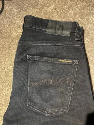 Nudie jeans - Säljer ett par mörk blåa Nudie Jeans. Klassisk femficksmodell med dragkedja och knapp i midjan. Jeansen har en stilren look. Hör av er vid frågor😀