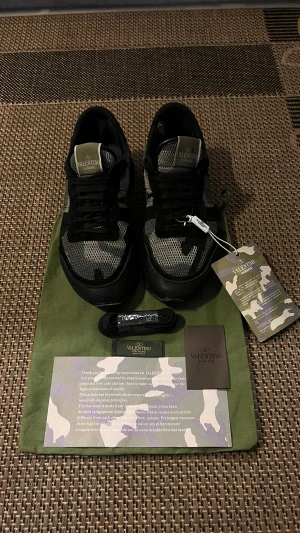 Valentino Garavani Rockrunner - Camo Design - Tjena! Säljer nu ett par exklusiva sneakers från det ikoniska italienska modehuset Valentino Garavani. 🏕️ skorna har inga fel endast lite defekt under skorna samt ett hål i hälen som inte påverkar något. •Tillbehör: Detta är ett fullset! Vid köp medföljer allt som syns på bilderna: • Original dustbag. • Extra skosnören (oöppnade) • Äkthetskort/Certifikat • Original tags Kom gärna med ett seriös bud!🤝