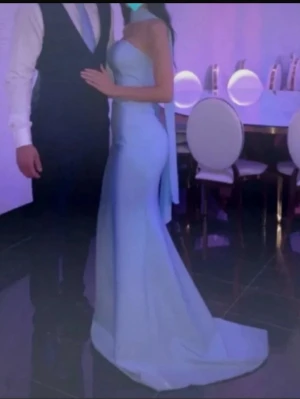 Ljusblå axelbandslös långklänning - Elegant ljusblå långklänning med axelbandslös design och figurnära passform. Klänningen har en släp baktill och markerad midja, vilket ger en stilren och sofistikerad look. Perfekt för speciella tillfällen.