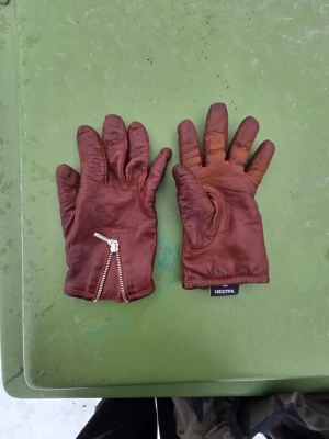 Bruna skinnhandskar från Hestra - Snygga bruna skinnhandskar från Hestra med dragkedja vid handleden och mjukt foder på insidan. Perfekta för kalla dagar och ger en stilren look. Klassisk design som passar till det mesta.