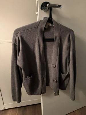 Brun kofta med stora knappar - Mysig brun  kofta med tre stora knappar framtill och praktiska fickor. Ena knappen är trasig men det finns en reserv som följer med. Koftan har en rak passform, långa ärmar och ribbade muddar. Perfekt att slänga över en t-shirt för en chill look.