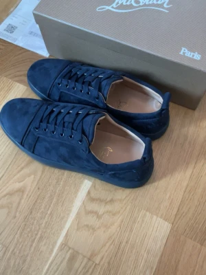 Svarta sneakers från Christian Louboutin - Säljer ett par svarta sneakers från Christian Louboutin med ikonisk röd sula och snygga detaljere Skorna har klassisk låg profil och är tillverkade i läder med svarta skosnören. Perfekt för dig som vill sticka ut med exklusiva skor. Kvitto finns och allt som tillkommer. Skriv vid intresse✌️