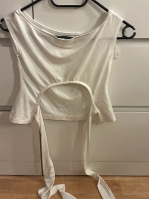 Vit croppad topp med knytband - Trendig vit croppad topp med breda knytband i midjan som ger en snygg siluett. Toppen har en enkel, stilren design och är ärmlös med rund halsringning. Perfekt att styla till jeans eller kjol för en cool look.