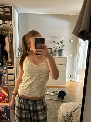 Randig vit och gul linnetopp - Säljer en söt randig linnetopp i vitt och ljusgult med smala axelband och v-ringad front. Toppen är ärmlös och har en slim passning, perfekt för varma dagar. Materialet känns som bomull och är mjukt mot huden.