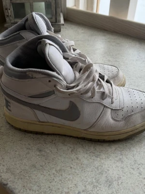 Vita Nike Sneakers - Ett par sneakers från Nike i vitt och grått. Skorna är i använt skick och är  smutsiga, för den som har ork till art göra rent så väntar det en betydligt fräschare sko.