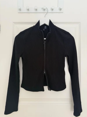 Svart zip cardigan  - En svart zip kofta. Dragkedjan kan justeras åt båda hållen. 