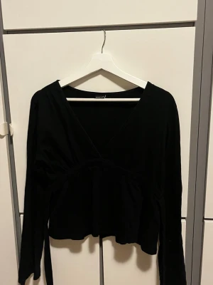 Svart topp med knytband - Snygg svart topp med långa ärmar och djup v-ringning. Toppen har knytband i midjan som ger en fin siluett. Perfekt att styla med höga jeans eller kjol för en trendig look.