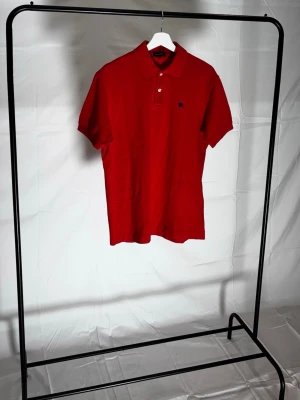 Röd pikétröja från Gant - Sick 8/10                                                                    Bra sick inga skador men användning syns på plagget. Klassisk röd pikétröja från Burberry med korta ärmar och krage. Tröjan har knappar vid halsen och en liten broderad logga på bröstet. Tillverkad i mjuk bomull som känns skön mot huden.