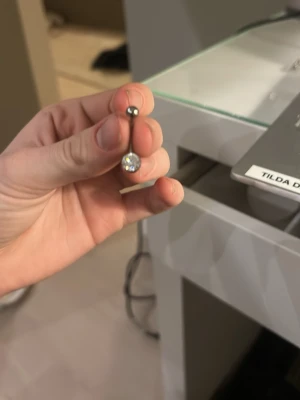 Silvrigt navelpercing med stor kristall - Snyggt silvrigt navelpercing med en stor, rund glittrande kristall och en mindre kula upptill. Perfekt för dig som gillar stilrena och glittriga accessoarer. Materialet ser ut att vara metall med en klar sten.