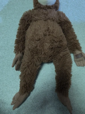 Brun mjuk apa gosedjur( känd som punch doll - Säljer ett gulligt gosedjur i form av en apa med mjuk, lurvig brun päls och beige ansikte, händer och fötter. Apan har långa armar och ben samt ett broderat leende på ansiktet. Perfekt som mysig kompis eller dekoration.