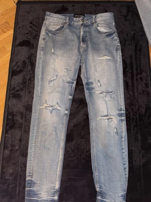 Ljusblå jeans från Supply and Demand - Säljer ett par ljusblå jeans från Supply and Demand  med slitningar och hål på både fram- och baksida. Jeansen har fem fickor, normal midja och raka ben. Perfekta för dig som gillar en avslappnad och trendig streetstil.