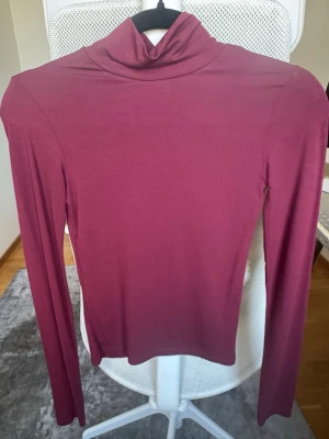 Vinröd polotopp med långa ärmar - Säljer en vinröd polotopp med lång ärm och tight passform. Toppen har en klassisk polokrage och är gjord i ett mjukt, stretchigt material som sitter snyggt på kroppen. Perfekt att styla med jeans eller kjol för en clean look.