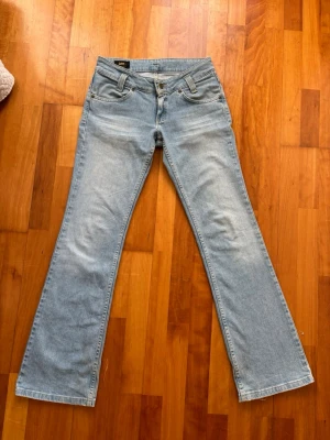 Ljusblå bootcut jeans från Lee - Säljer ett par ljusblå bootcut jeans från Lee med klassisk femficksdesign och dragkedjegylf. Jeansen har en snygg tvättad look och Lee-logga på bakfickan. Perfekta för dig som gillar retrostil och vill ha ett par bekväma jeans i bomull.💓
