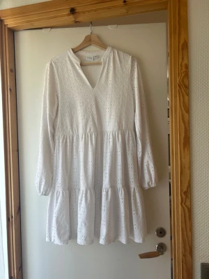 Vit broderad kortklänning från Vila - Söt vit kortklänning från Vila med broderade detaljer och v-ringning. Klänningen har lång ärm, volang i kjolen och är tillverkad i bomull. Perfekt för sommarens alla tillfällen!