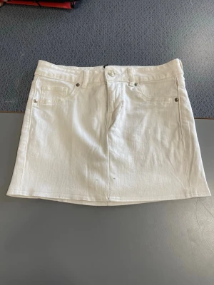 Vit jeanskjol med fickor - Snygg vit jeanskjol med klassiska fickor fram och knappstängning i midjan. Kjolen har en rak, kort passform och är perfekt för en trendig vardagslook. Passar till allt och är enkel att styla med olika toppar.