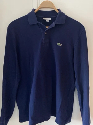 Mörkblå Lacoste Rugbytröja - Klassisk mörkblå långärmad rugbytröja från Lacoste. Väldigt bra skick.