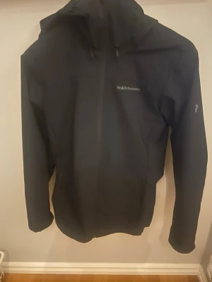 Svart vindjacka från Peak Performance !pris kan diskuteras! - Snygg svart vindjacka från Peak Performance med huva och dragkedja framtill. Jackan har minimalistisk design, diskret logga på bröstet och är tillverkad i ett lätt, vindtätt material som passar perfekt för blåsiga dagar. Den är knappt nom är i nyskick. Pris kan diskuteras och hör v er vid eventuella frågor