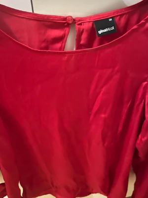 Röd blus från Gina Tricot - Snygg röd blus från Gina Tricot med rund halsringning och knapp i nacken. Blusen har lång ärm och är gjord i ett glansigt, mjukt material som ger en elegant känsla. Perfekt att styla med jeans eller kjol för en trendig look.