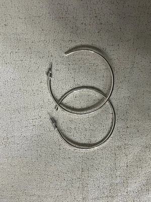Stora silvriga hoops örhängen - Säljer ett par stora, klassiska hoops i silverfärgad metall. Örhängena har en enkel och stilren design utan dekorationer, perfekta för dig som gillar minimalistiska accessoarer. Passar till många olika looks och är lätta att matcha.