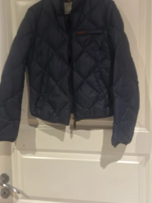 Mörkblå quiltad pufferjacka - Snygg mörkblå pufferjacka med quiltat mönster och dragkedja framtill. Perfekt nu till våren, storlek xs