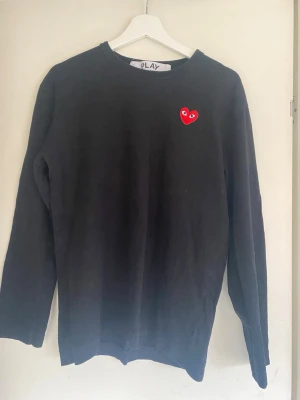 Svart tröja Comme des Garçons Play - Svart långärmad tröja från Comme des Garçons Play med det ikoniska röda hjärtat med ögon broderat på bröstet. Tröjan har rund halsringning och är tillverkad i mjukt bomullsmaterial. Perfekt för en stilren och trendig look. Passar i M också 