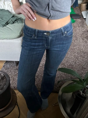 Blå bootcut jeans med låg midja - Säljer ett par blå bootcut jeans med låg midja och snygga kontrastsömmar. Jeansen har klassiska fem fickor och coola broderade detaljer på bakfickorna. Perfekta för dig som gillar en avslappnad men trendig look.