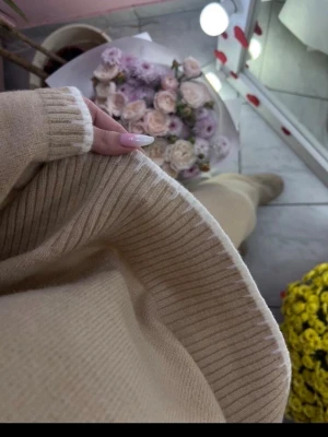 Beige stickat loungewear-set - Mysigt loungewear-set i beige stickad kvalitet med ribbade muddar på både tröja och byxor. Setet har en avslappnad passform och är perfekt för hemmamys. Materialet ser ut att vara mjukt och stretchigt, vilket ger extra komfort.