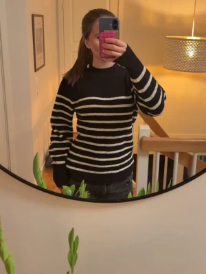 Svartvit randig stickad tröja - Säljer en svart stickad tröja med vita horisontella ränder och dekorativa glittriga knappar på ena axeln. Tröjan har rund halsringning och långa ärmar. Perfekt för dig som gillar klassisk men ändå trendig stil.