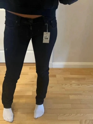 Mörkblå skinny jeans med stretch - Snygga mörkblå skinny jeans med klassisk femficksdesign och kontrastsömmar. Jeansen har låg midja och är tillverkade i ett stretchigt material för en bekväm passform. Perfekta till en avslappnad eller trendig look. I storleken 27/34