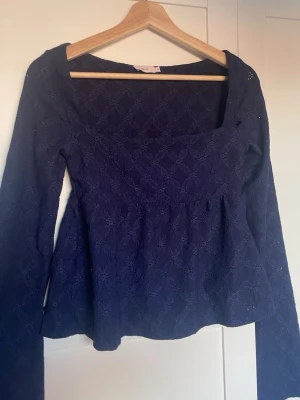 Mörkblå spetsblus från Nelly - Supersnygg mörkblå blus från Nelly med lång ärm och spetsdetaljer. Blusen har en fyrkantig ringning och markerad midja som ger en feminin siluett. Perfekt att styla med jeans eller kjol för en trendig look.