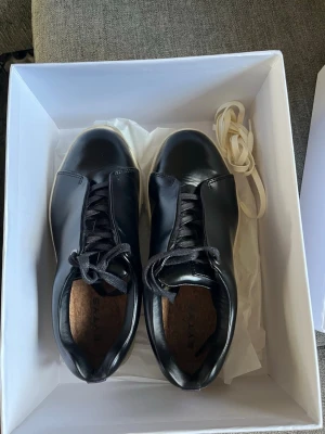 Svarta sneakers från Eytys - Stilrena svarta sneakers från Eytys med slät ovandel i blankt läder och vita sulor. Skorna har svarta skosnören och extra vita snören medföljer. Klassisk låg modell med rund tå och diskret branding på innersulan. Endast använda ett par gånger, nästan som nya. 